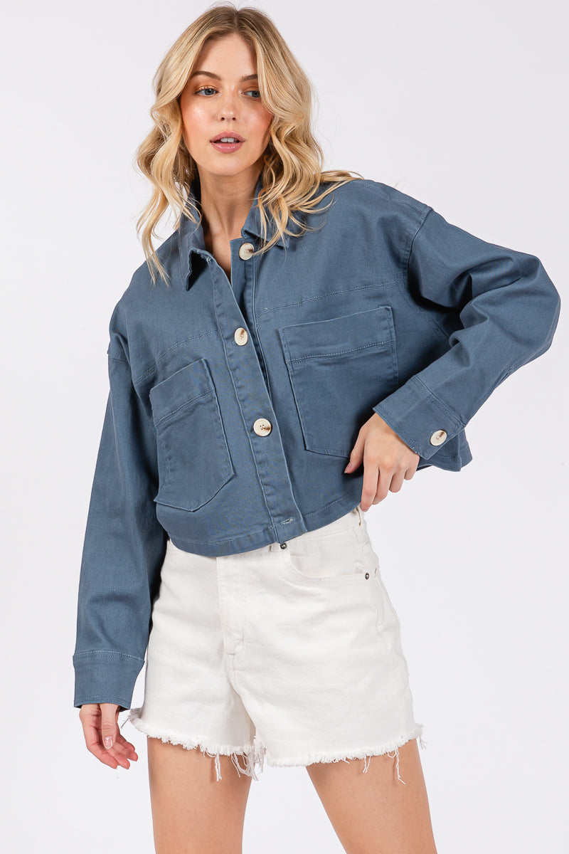 Cropped denim-style jacket with button-down front and oversized buttons, paired with white shorts for a chic look.